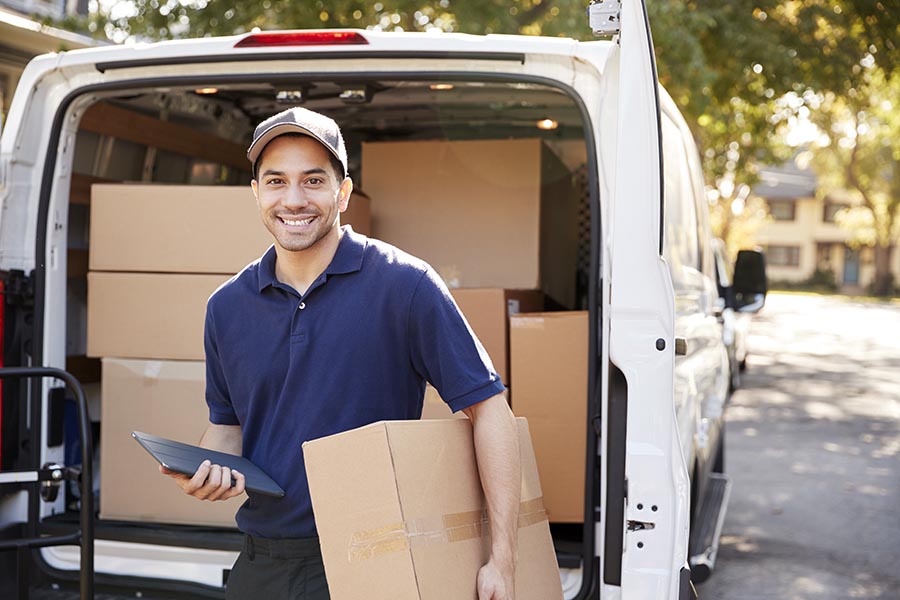 Business Insurance - Courier Smiles as He Prepares to Deliver a Package, a Large White Van Filled With Product Behind Him